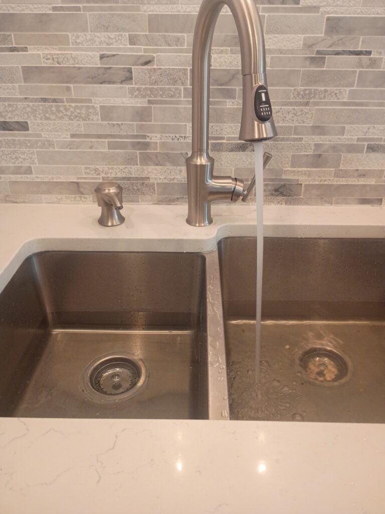 How Much Does It Cost to Repipe a House in Florida? 2 Modern stainless steel kitchen double sink with a pull-down faucet running water into the right basin, showcasing clean plumbing installation, water flow testing, and a tiled backsplash in a newly finished kitchen.