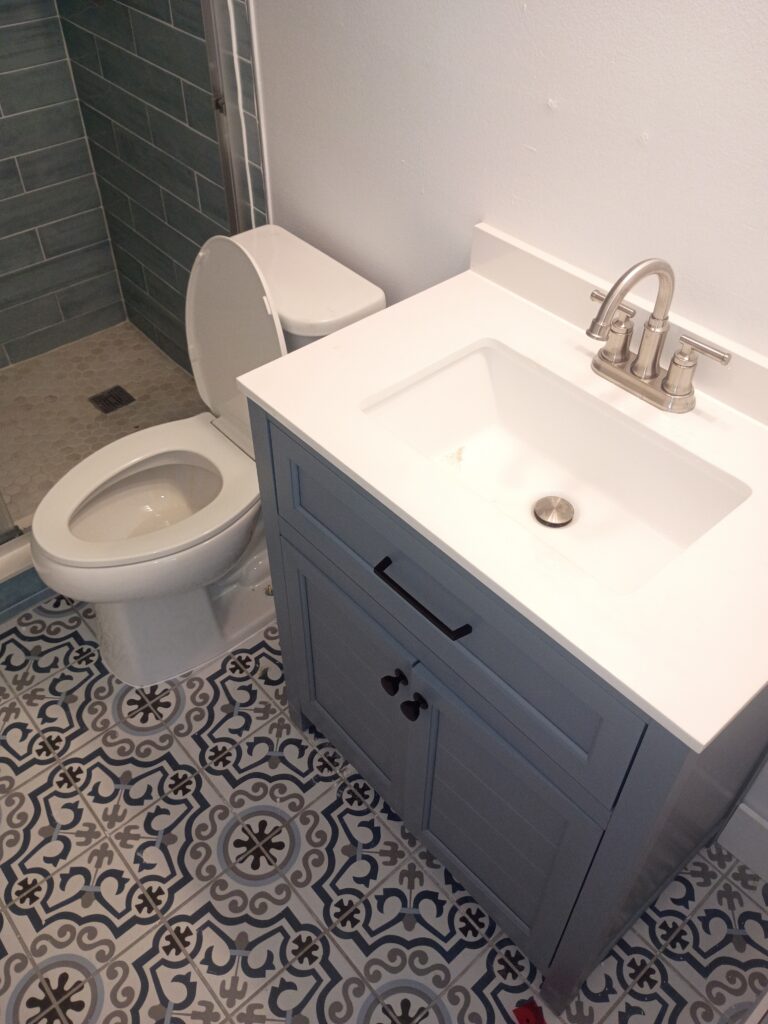 How Much Does It Cost to Repipe a House in Florida? 3 Modern bathroom interior featuring a newly installed white vanity with quartz countertop, stainless steel faucet, and integrated sink beside a toilet and glass shower. The space includes patterned tile flooring and fresh finishes, highlighting a clean bathroom plumbing installation and remodel.