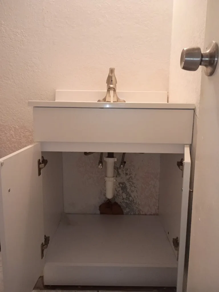 sewer line installation on trench White bathroom vanity with open doors showing a newly repaired PVC P-trap drain pipe and faucet lines by a local plumber in Largo, FL.