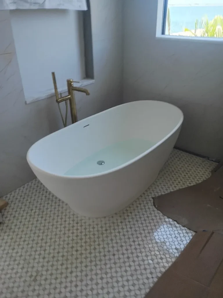 sewer line installation on trench Modern white freestanding oval bathtub featuring a luxury floor-mounted gold faucet on mosaic tile flooring in Largo, Florida.