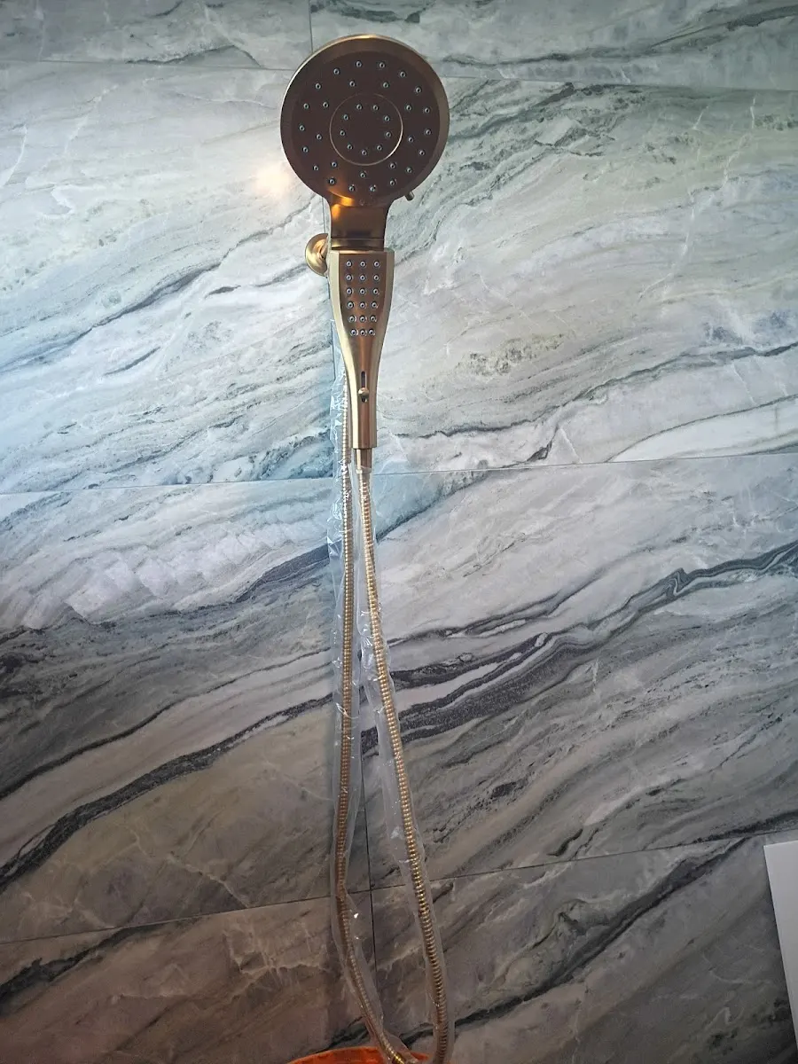 Elegant gold handheld shower head with a flexible hose installed against a luxury gray marble-tiled wall in Largo, FL.