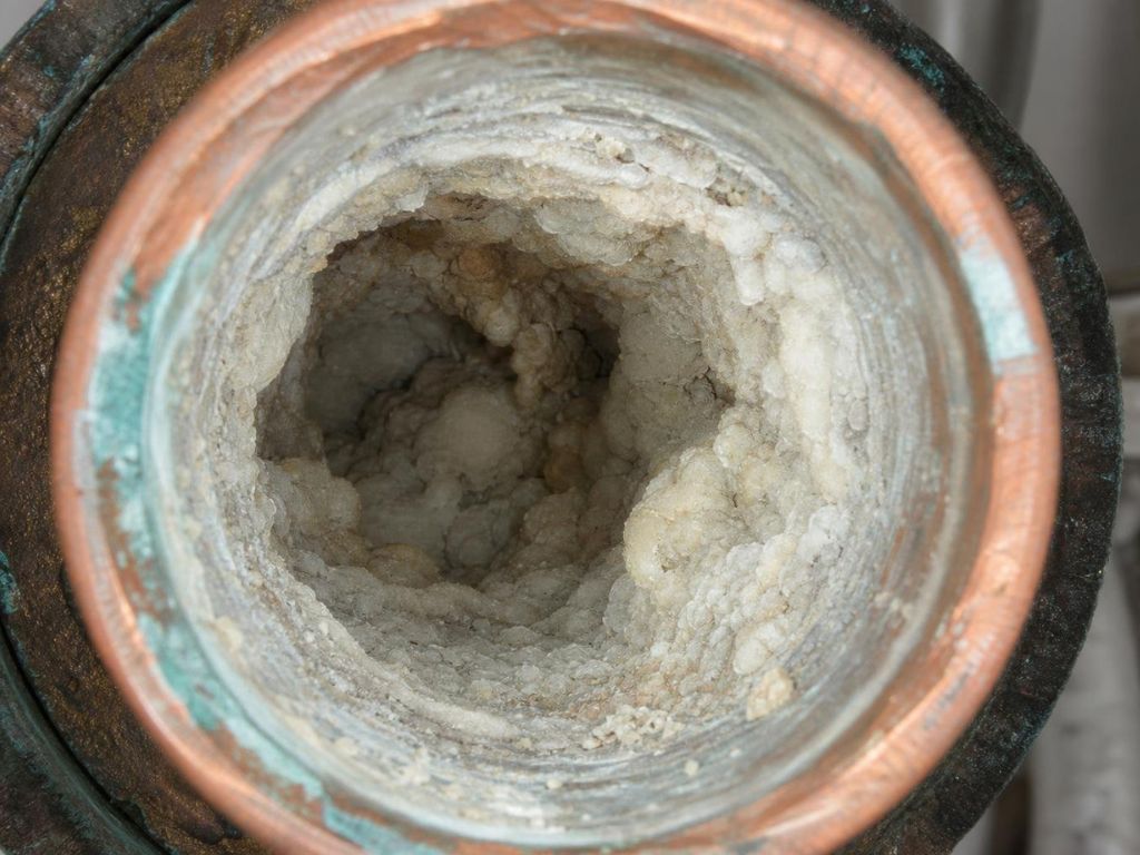 user-inserted Close-up view of severe mineral scale buildup inside a copper water heater pipe, showing heavy deposits that restrict water flow and reduce efficiency, highlighting the need for professional water heater maintenance and descaling.