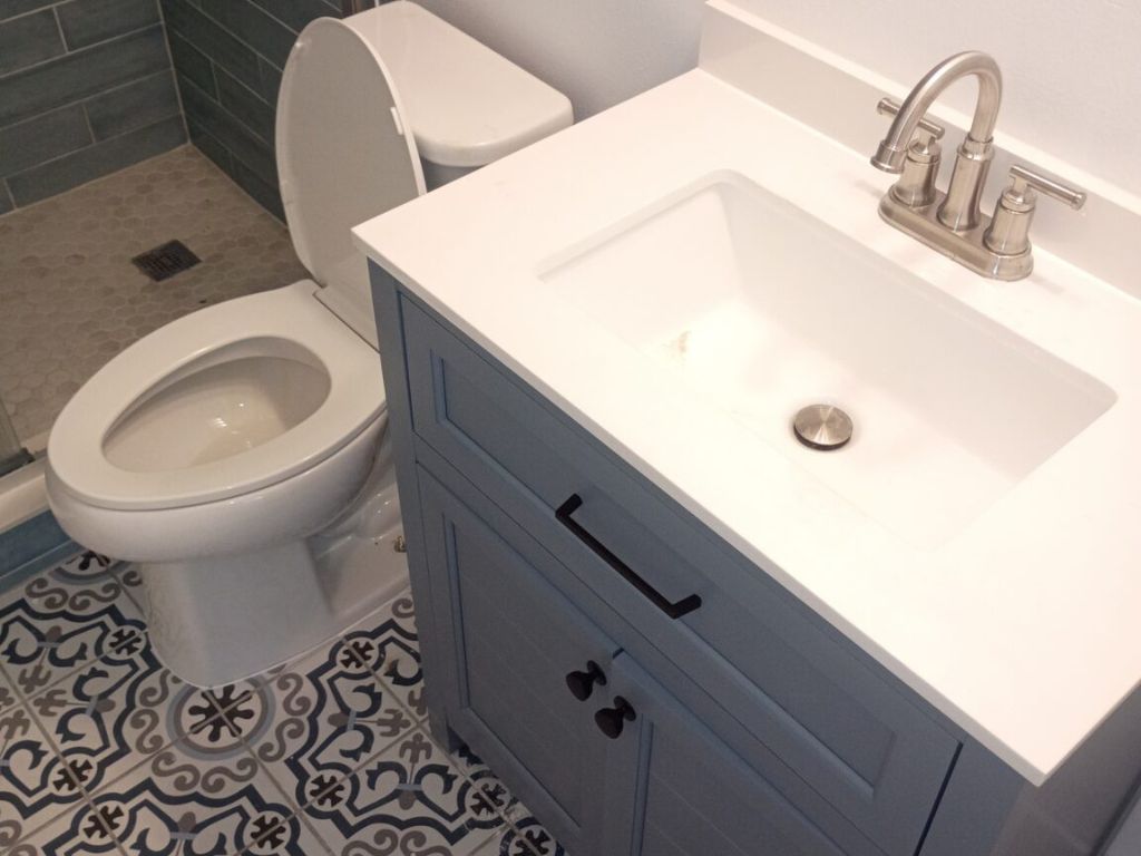 How Much Does It Cost to Repipe a House in Florida? 3 Modern bathroom interior featuring a newly installed white vanity with quartz countertop, stainless steel faucet, and integrated sink beside a toilet and glass shower. The space includes patterned tile flooring and fresh finishes, highlighting a clean bathroom plumbing installation and remodel.