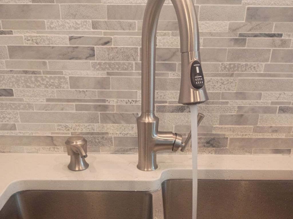 How Much Does It Cost to Repipe a House in Florida? 2 Modern stainless steel kitchen double sink with a pull-down faucet running water into the right basin, showcasing clean plumbing installation, water flow testing, and a tiled backsplash in a newly finished kitchen.