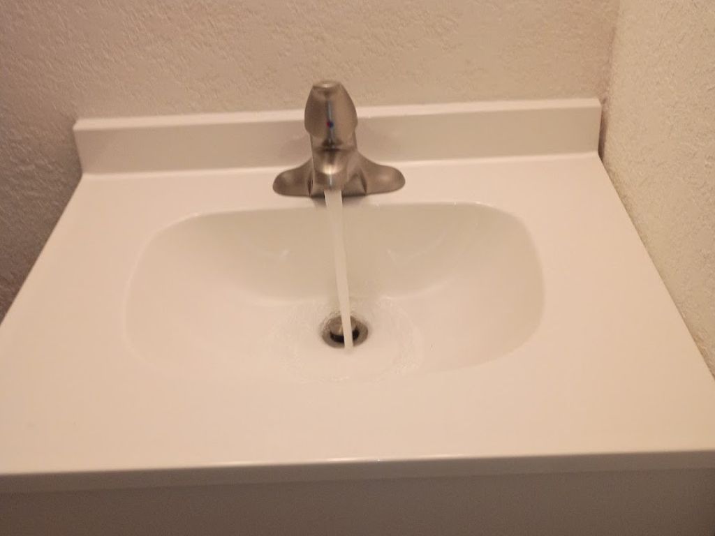 Bathroom sink faucet running water into a drain after shutting off main supply during a burst pipe plumbing emergency.