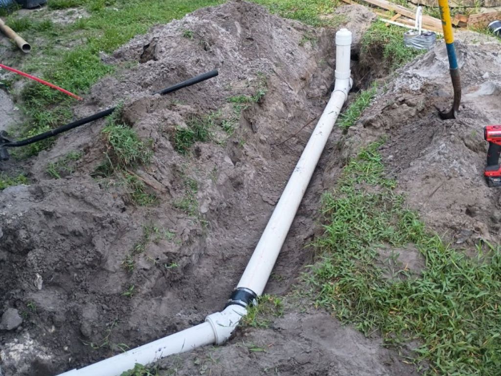 Excavated yard with new sewer pipe installation, showing underground plumbing repair after sewer line damage or root intrusion.