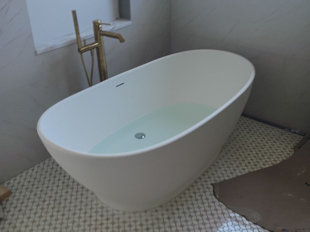 Freestanding bathtub with standing water from a clogged drain, showing need for shower drain snaking or plumbing service.